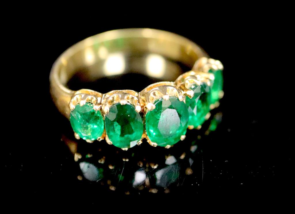 A mid to late 20th century gold and graduated five stone oval cut emerald set half hoop ring,